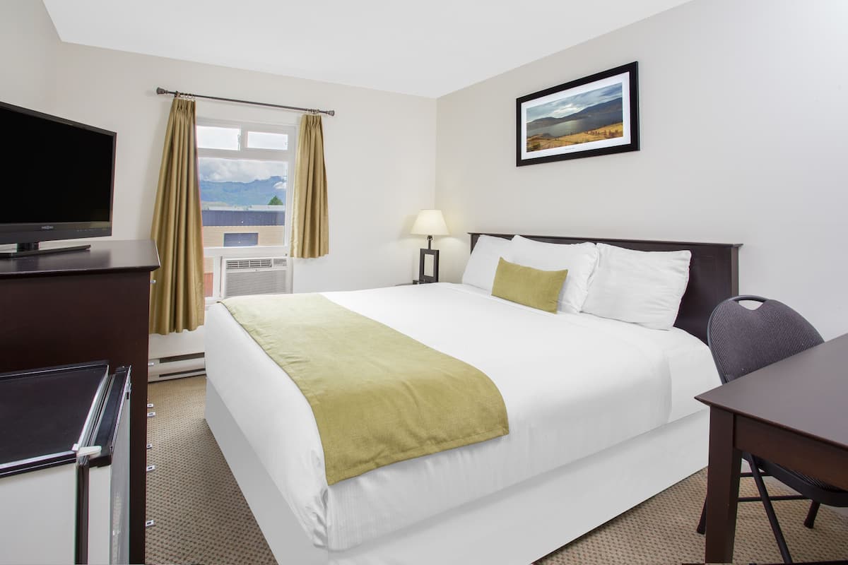 A hotel room with a bed, a desk, a TV, a lamp, and a picture on the wall.