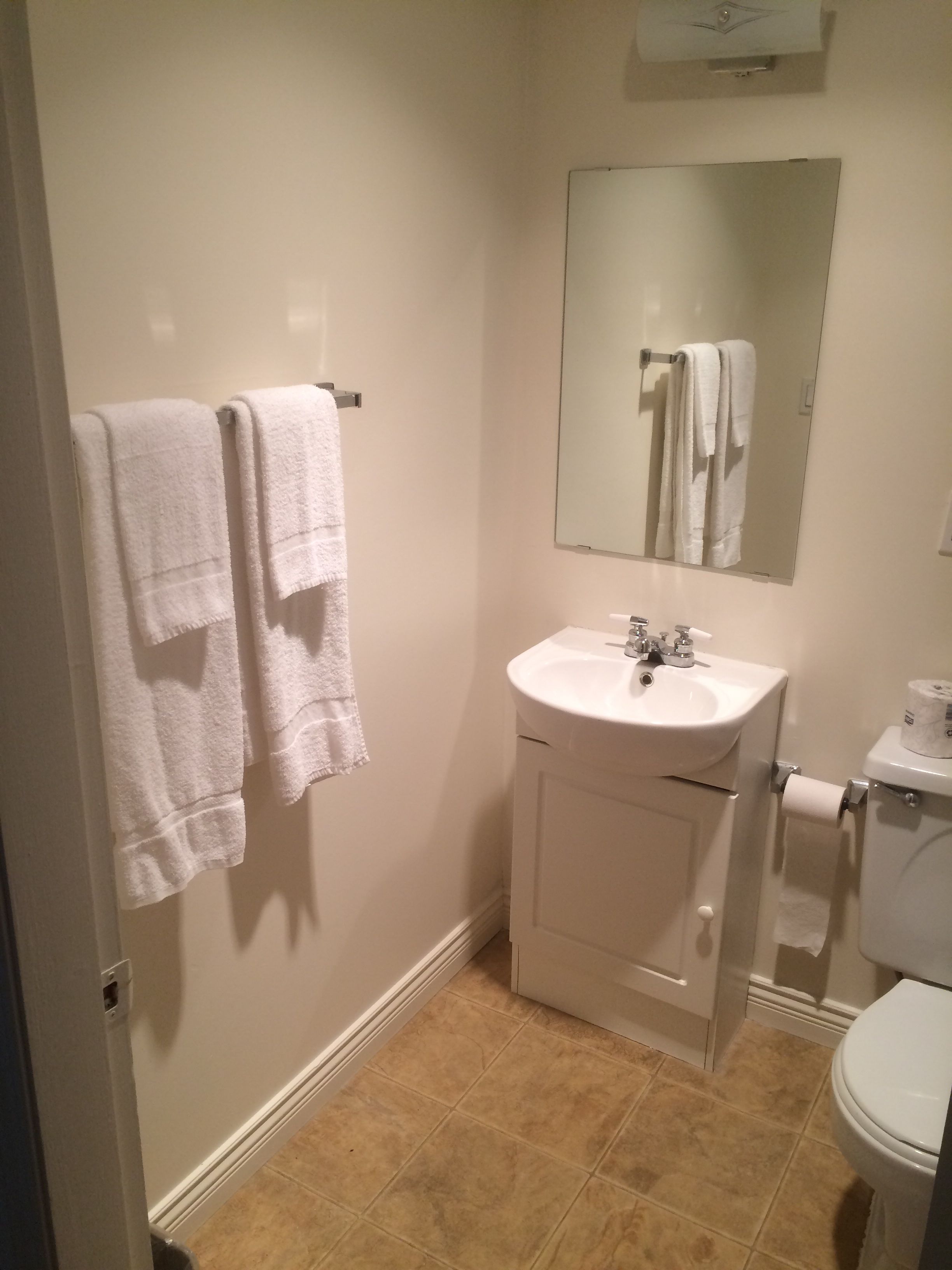 A bathroom with a sink, mirror, and toilet. There are two towels hanging on a rack.