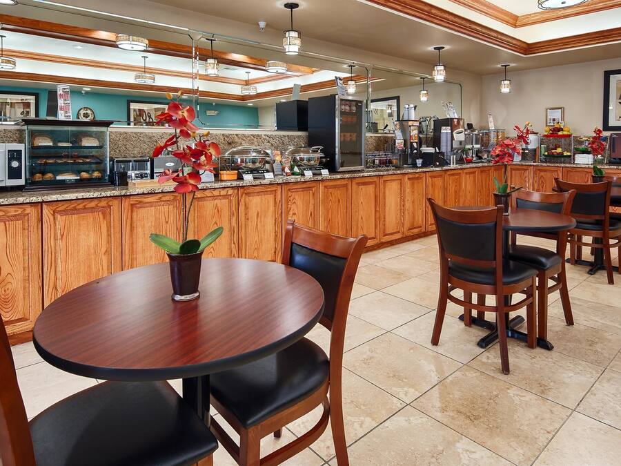 A hotel kitchen with wooden cabinets, a central island with food display, and a seating area with tables and chairs.