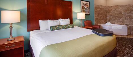 A hotel room with a large bed, two bedside lamps, a wooden nightstand, a red leather chair, a small table with a towel, and a stone-textured wall.