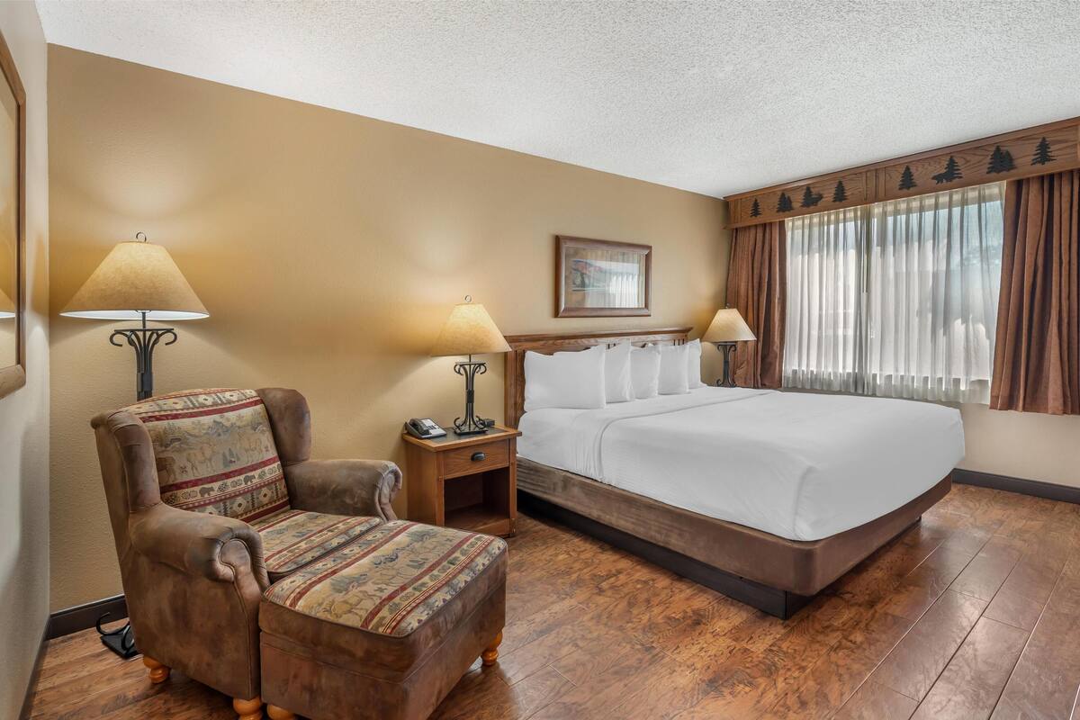 A hotel room with a large bed, a chair, two bedside tables with lamps, and a window with curtains.