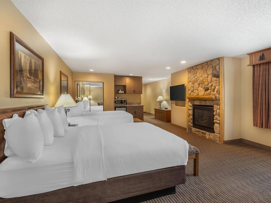 A hotel room with two beds, a stone fireplace, a TV, and a desk with a lamp.