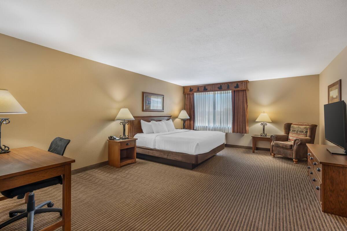 A hotel room with a large bed, two bedside tables with lamps, a desk with a chair, and a television.