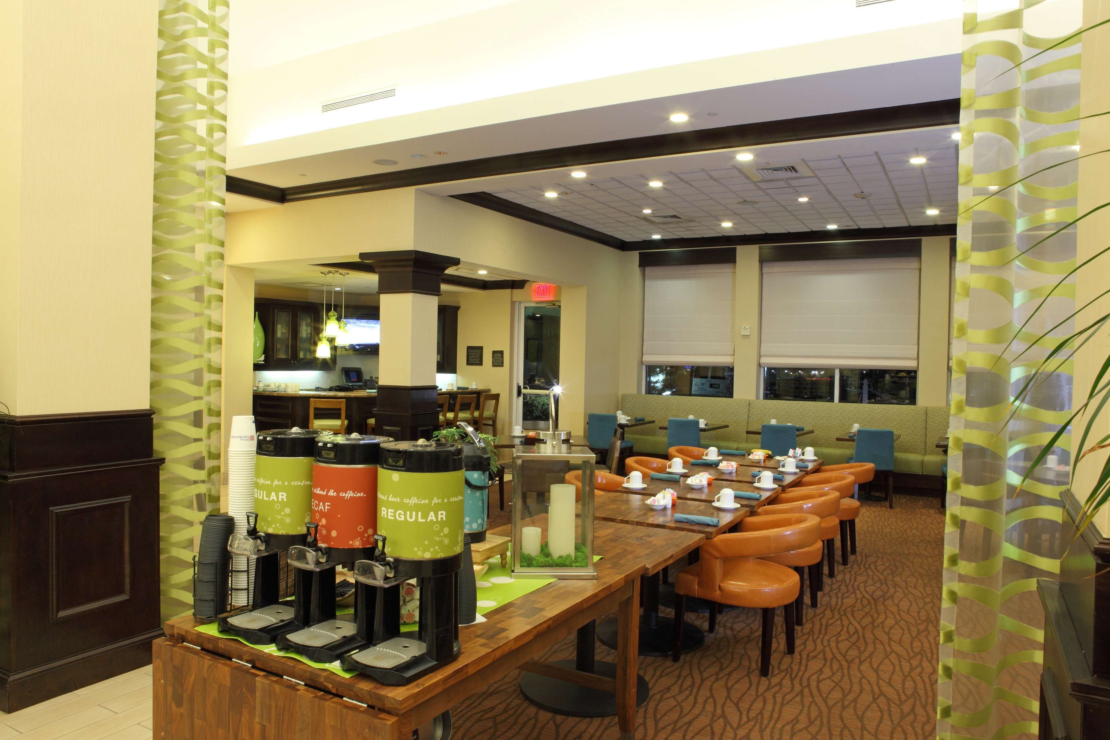 A hotel dining area with a buffet setup, including coffee and juice dispensers, and a seating arrangement with tables and chairs.
