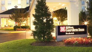 A Hilton Garden Inn Frederick building entrance with a sign, a lawn, and a tree. - Hilton Garden Inn Frederick (Frederick)