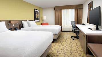 A hotel room with two beds, a desk, a chair, a TV, and a window with curtains.
