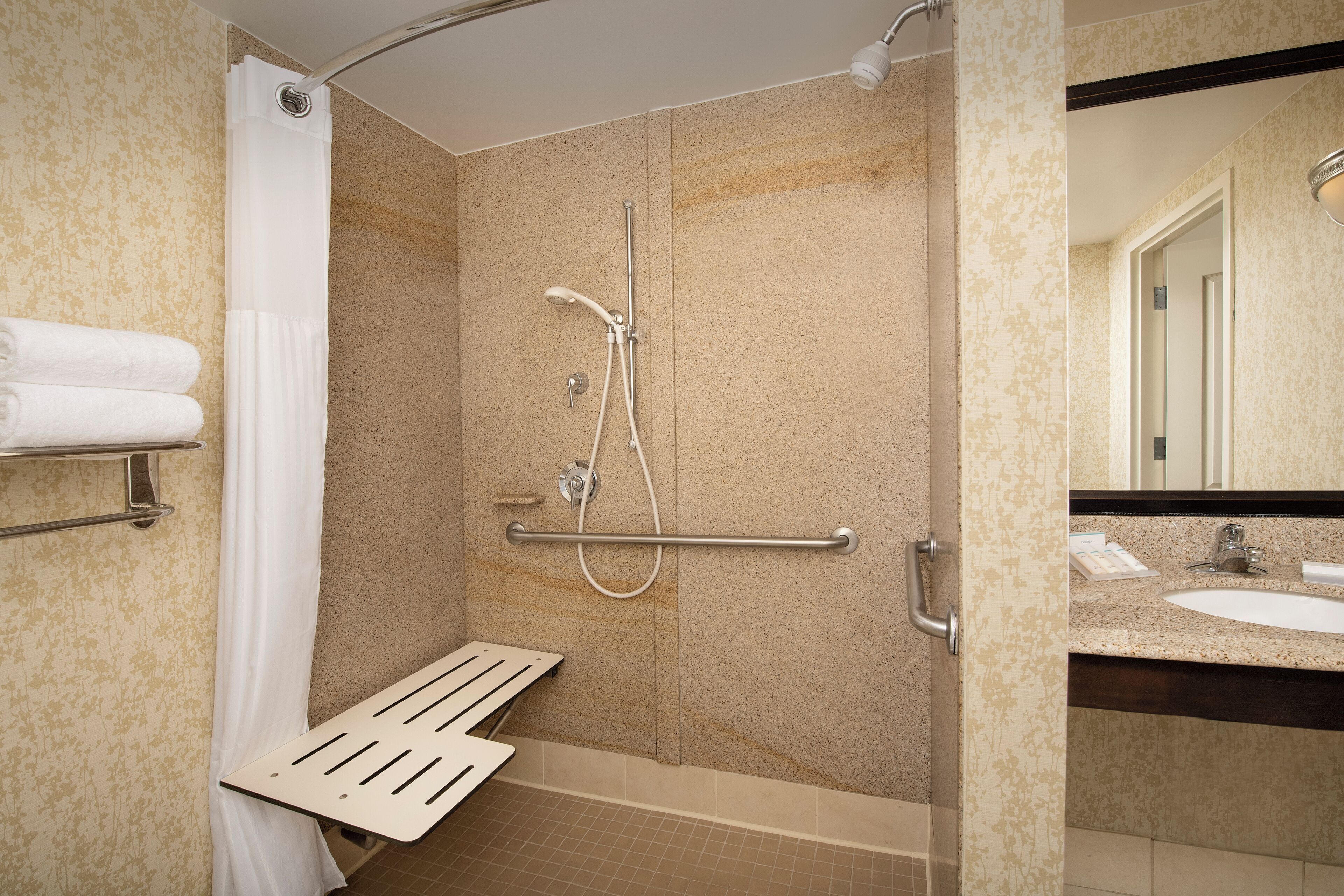 A shower with a grab bar, a towel rack, and a sink with a mirror.