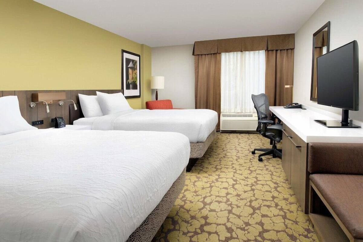 A hotel room with two beds, a desk with a computer, a chair, and a window with curtains.