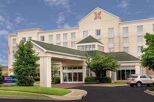 A hotel with a clear entrance, a sign indicating it's a Hilton Garden Inn, and a parking area with a vehicle.