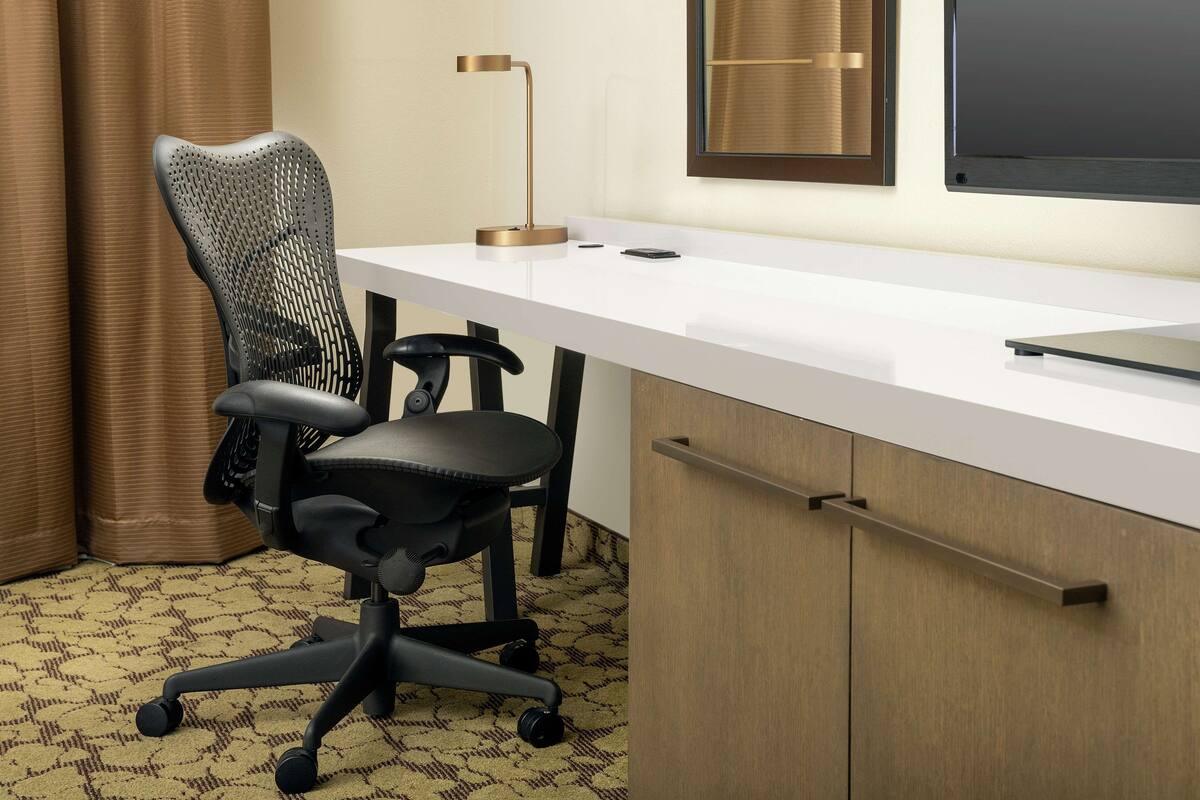 A modern office desk with a chair, a lamp, and a computer monitor.