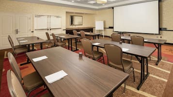 Een congrescentrum met meerdere tafels en stoelen, een whiteboard, een projectiescherm en een vloerbedekking.