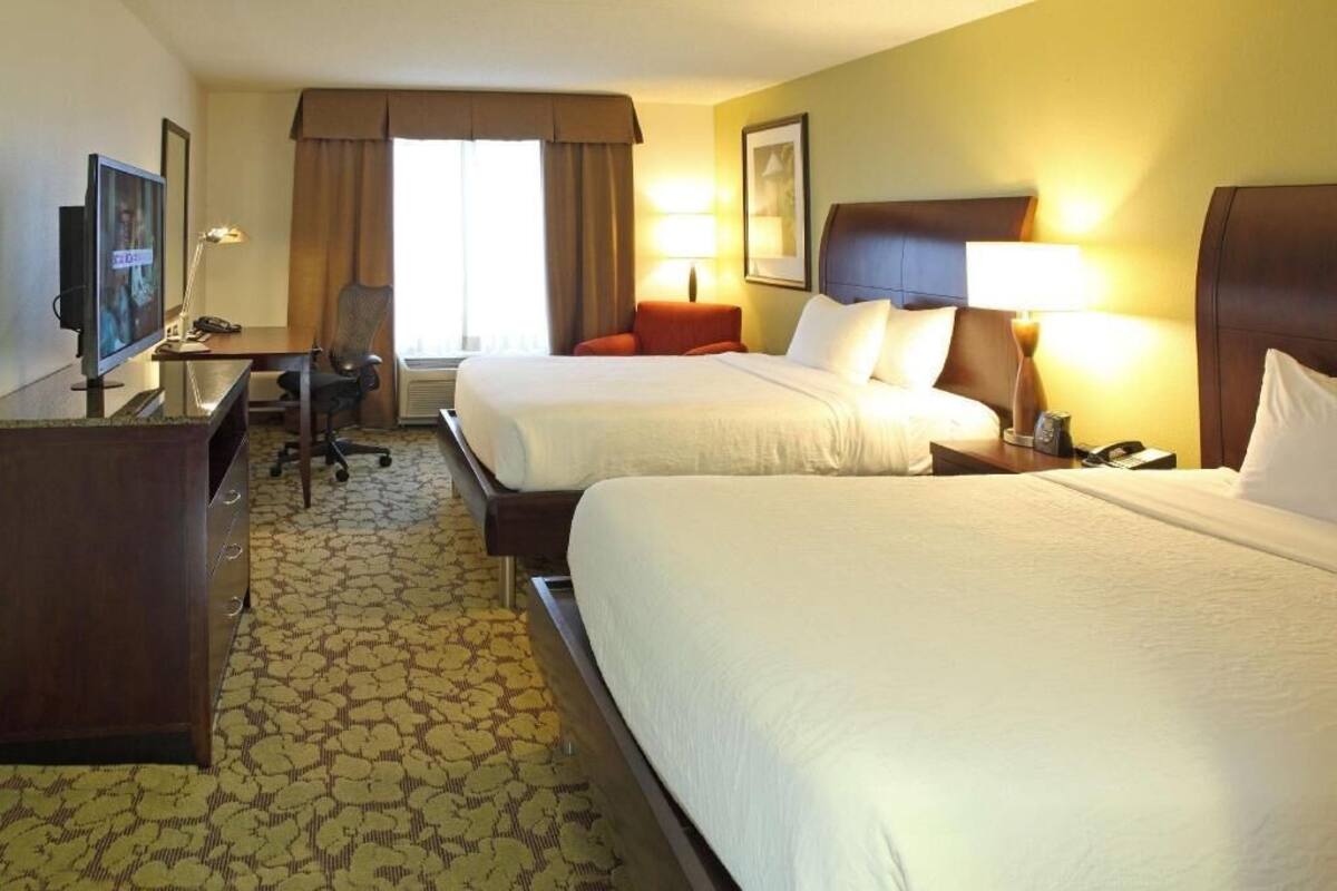 A hotel room with two beds, a desk with a chair, a television, and a lamp.