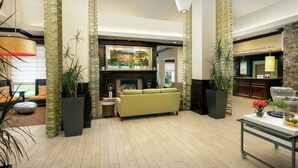 A spacious lobby with a green sofa, a fireplace, and large potted plants. - Hilton Garden Inn Frederick (Frederick)