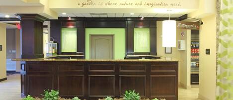 A reception area with a dark wood counter, green upholstered seating, and a wall with a nature-themed quote.
