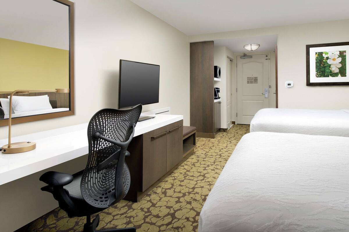 A hotel room with a bed, a desk with a chair, a television, and a door leading to another room.