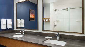 A modern bathroom with two sinks, a large mirror, and a glass shower enclosure.