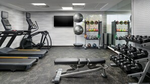 Un gimnasio con cintas de correr, una prensa de banca y un estante con mancuernas.