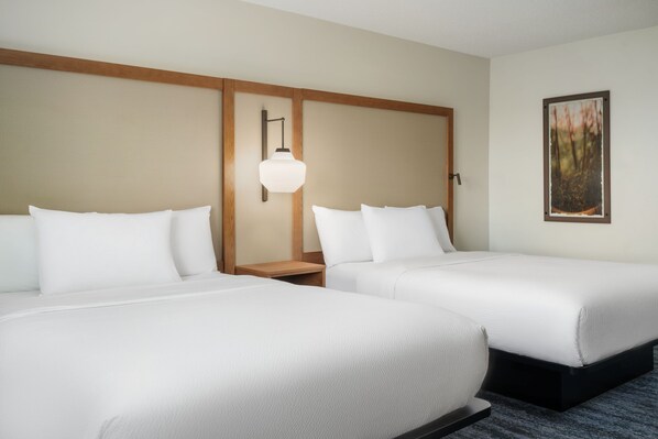A hotel room with two single beds, a nightstand, a wall-mounted lamp, and a framed picture on the wall.