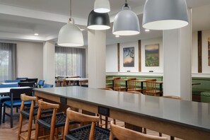 A modern dining area with a long counter, wooden chairs, and pendant lighting.