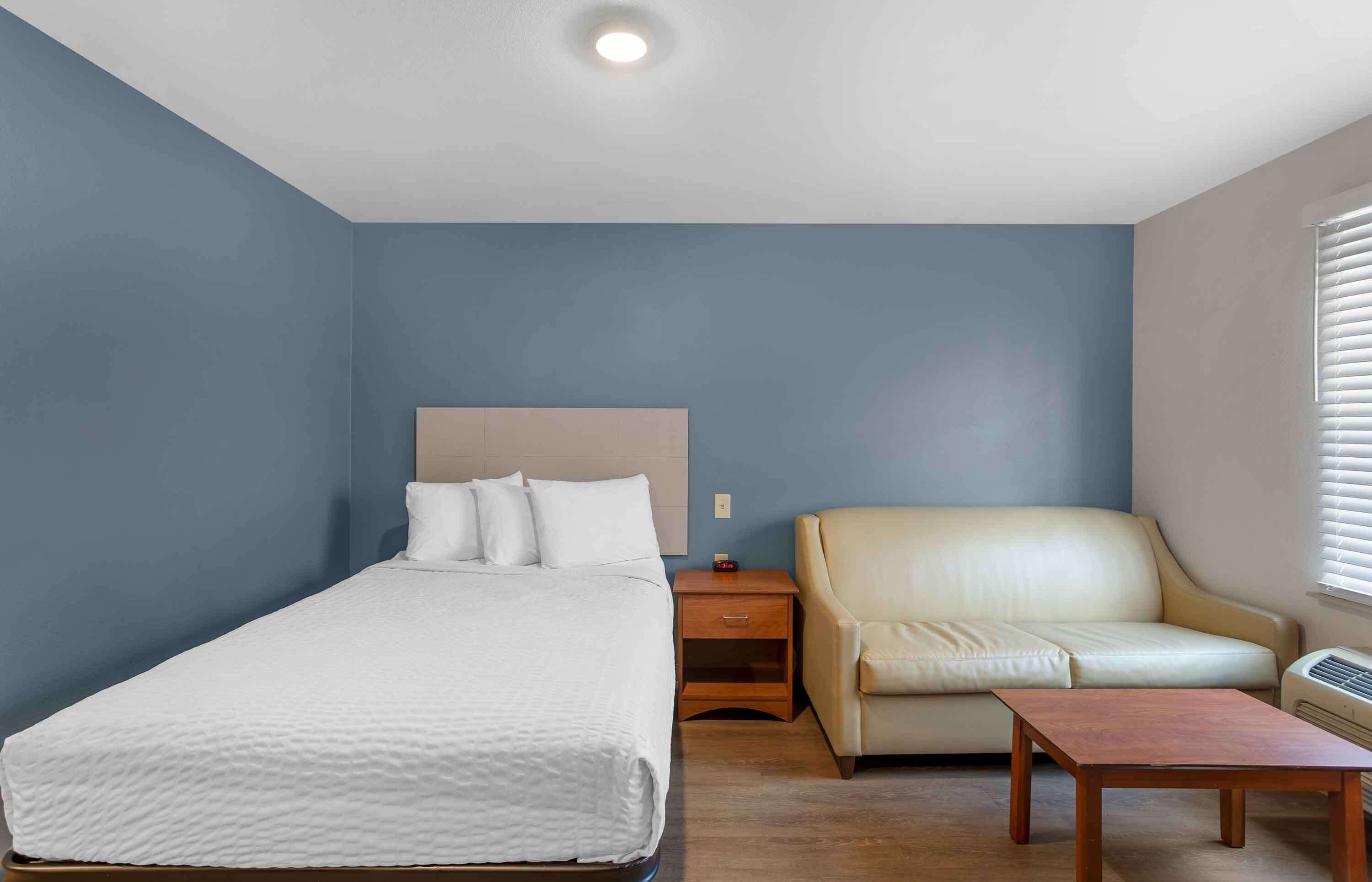 Una habitación de hotel con una cama individual, una mesita de noche, un sillón de cuero y una mesa de madera.