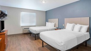 A hotel room with two beds, a TV, a heater, and a window with blinds. - Extended Stay America Select Suites - Springfield - South - Battlefield (Springfield)