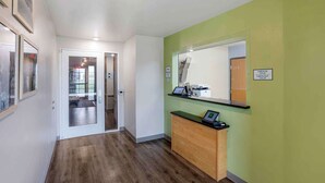 A reception area with a glass door leading to a room, a reception desk with a computer, and a green wall. - Extended Stay America Select Suites - Springfield - South - Battlefield (Springfield)