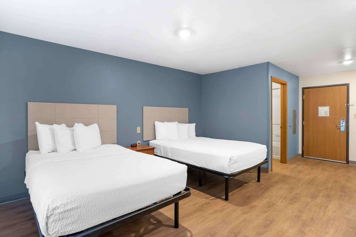A hotel room with two single beds, a wooden floor, and a blue wall.