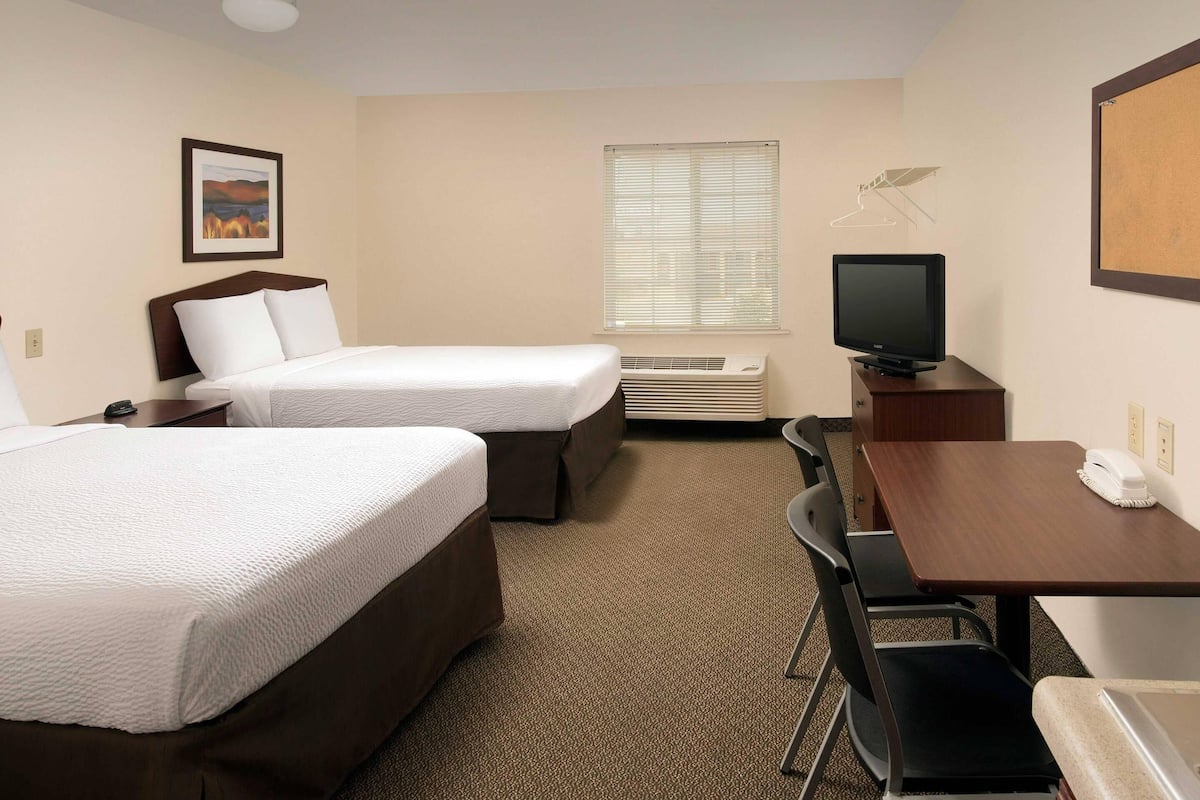 A hotel room with two beds, a desk with a telephone, a television, and a window with blinds.