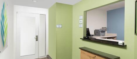 A reception area with a green wall, a wooden counter, a computer, and a printer.