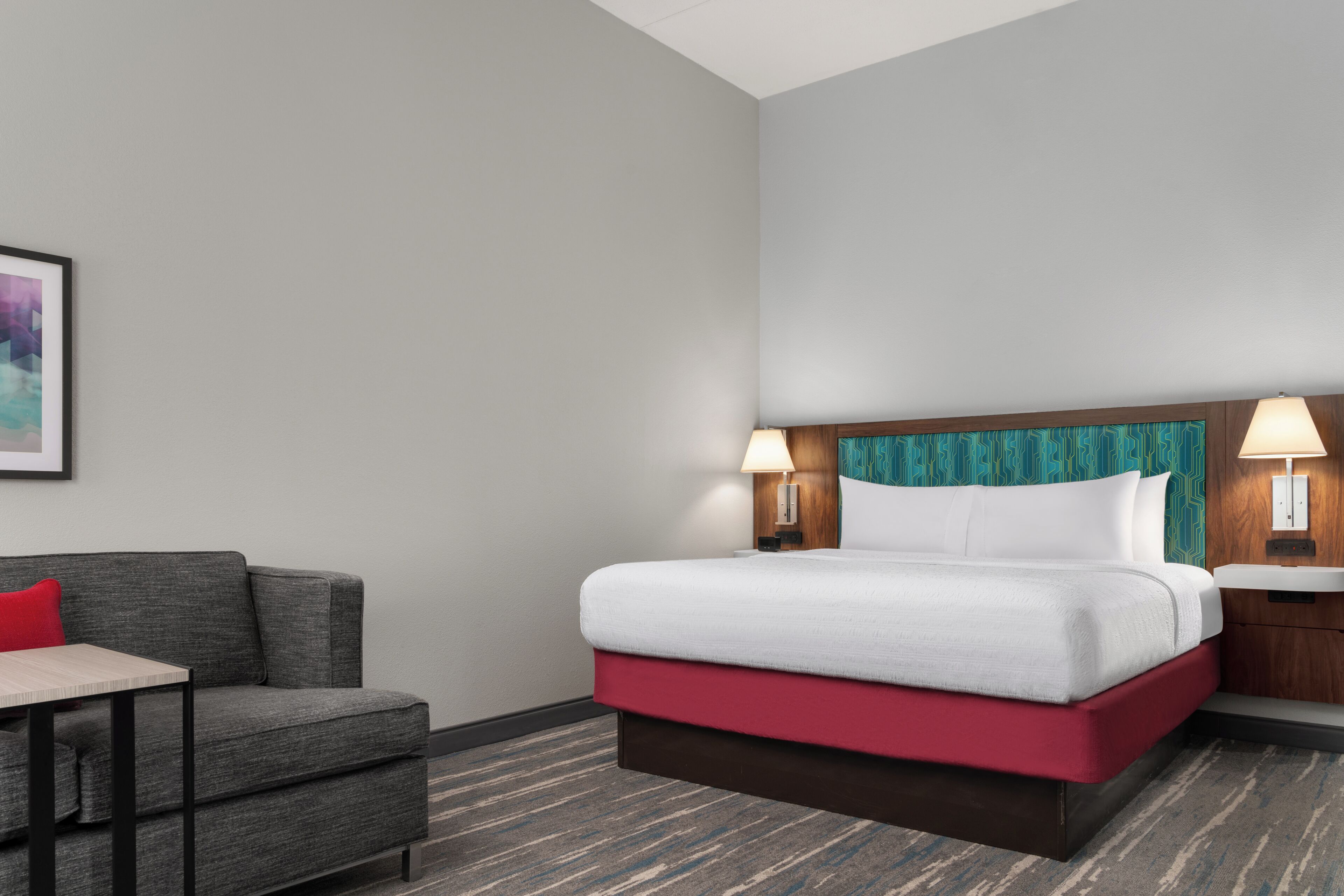 A hotel room with a bed, a desk, a chair, and two wall-mounted lamps.
