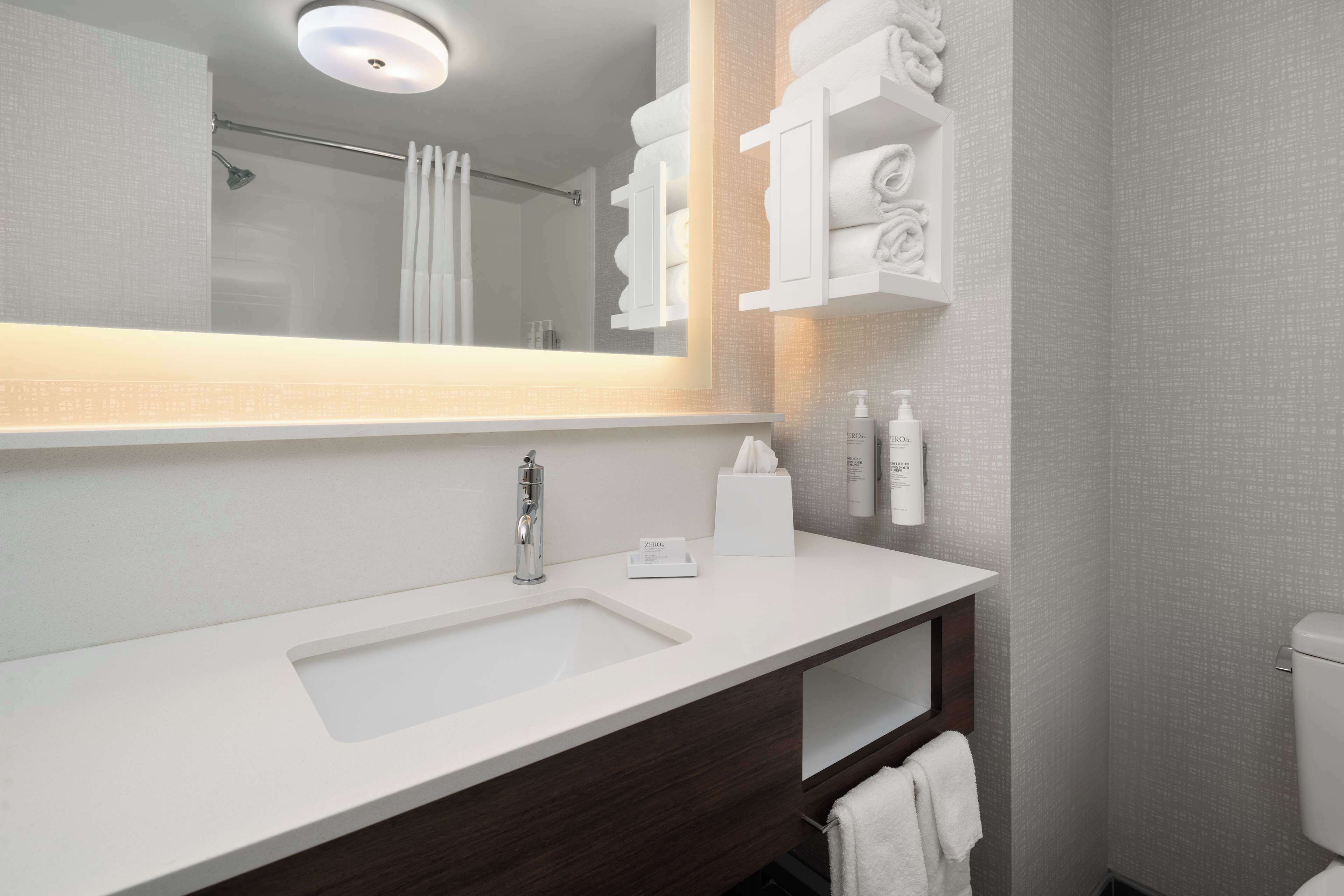 A modern bathroom with a large mirror, white sink, and towel storage.
