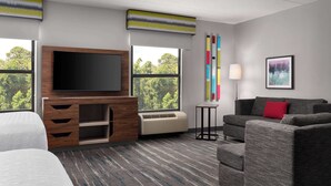 A hotel room with a large flat-screen TV, a sofa, a bed, a small table, and a window with a view of trees. - Hampton Inn Spring Lake Fayetteville (Spring Lake)