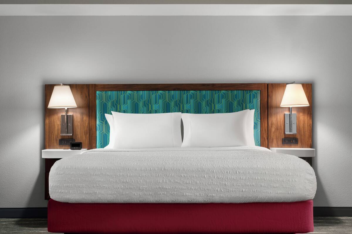 Ein Hotelzimmer mit einem großen Bett, zwei Nachttischen mit Lampen, einem hölzernen Kopfteil und einer Wand mit blaugrünem Muster.