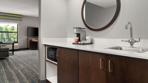 A modern bathroom with a white countertop, a round mirror, a sink, and a coffee maker. - Hampton Inn Spring Lake Fayetteville (Spring Lake)