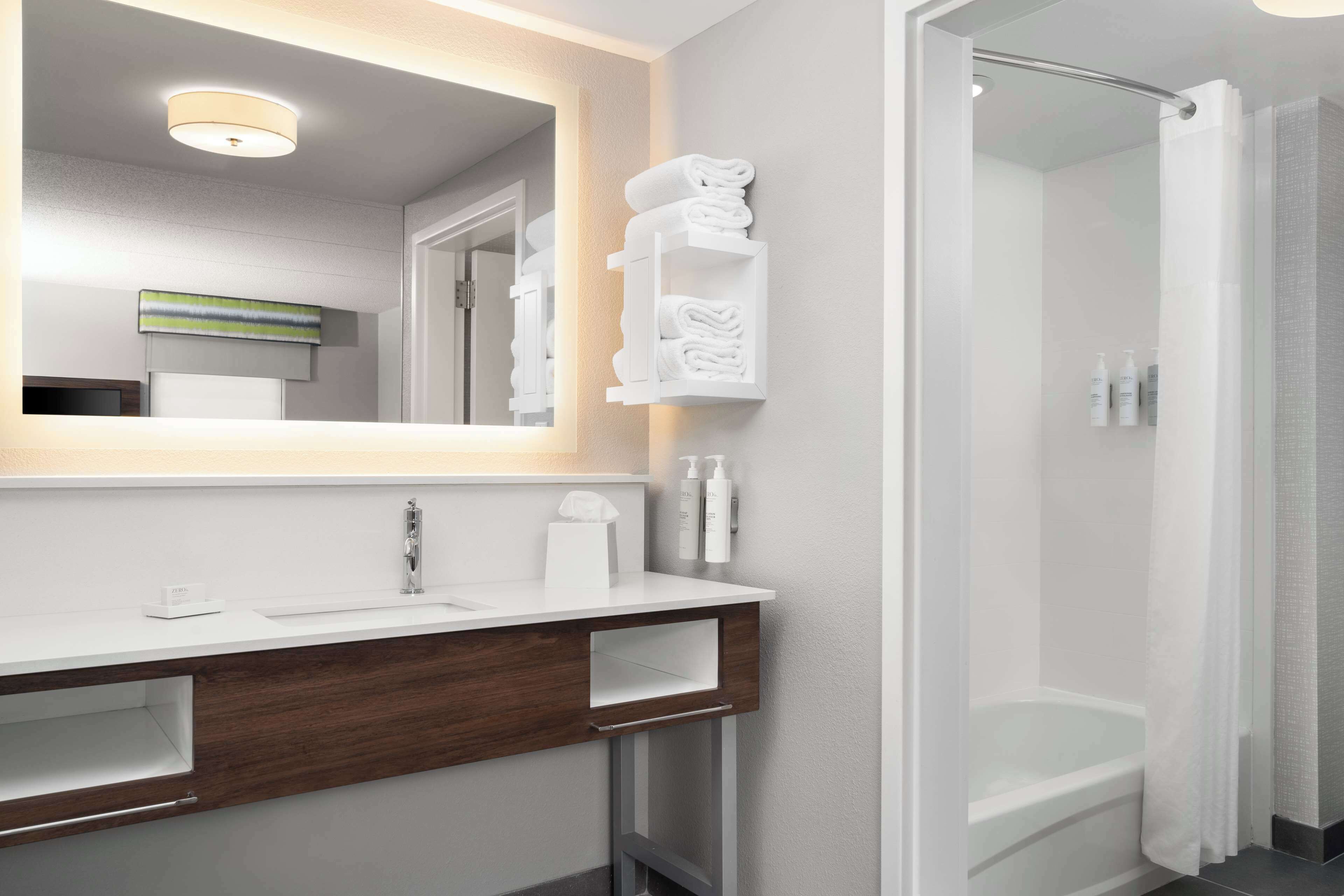 A modern bathroom with a white vanity, a large mirror, a shower enclosure, and a towel rack.