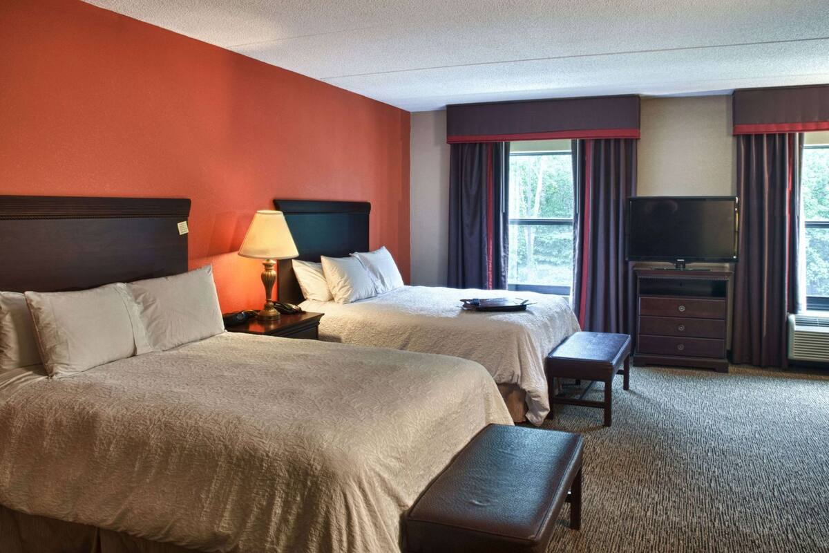 A hotel room with two beds, a TV, a desk, and a window with curtains.