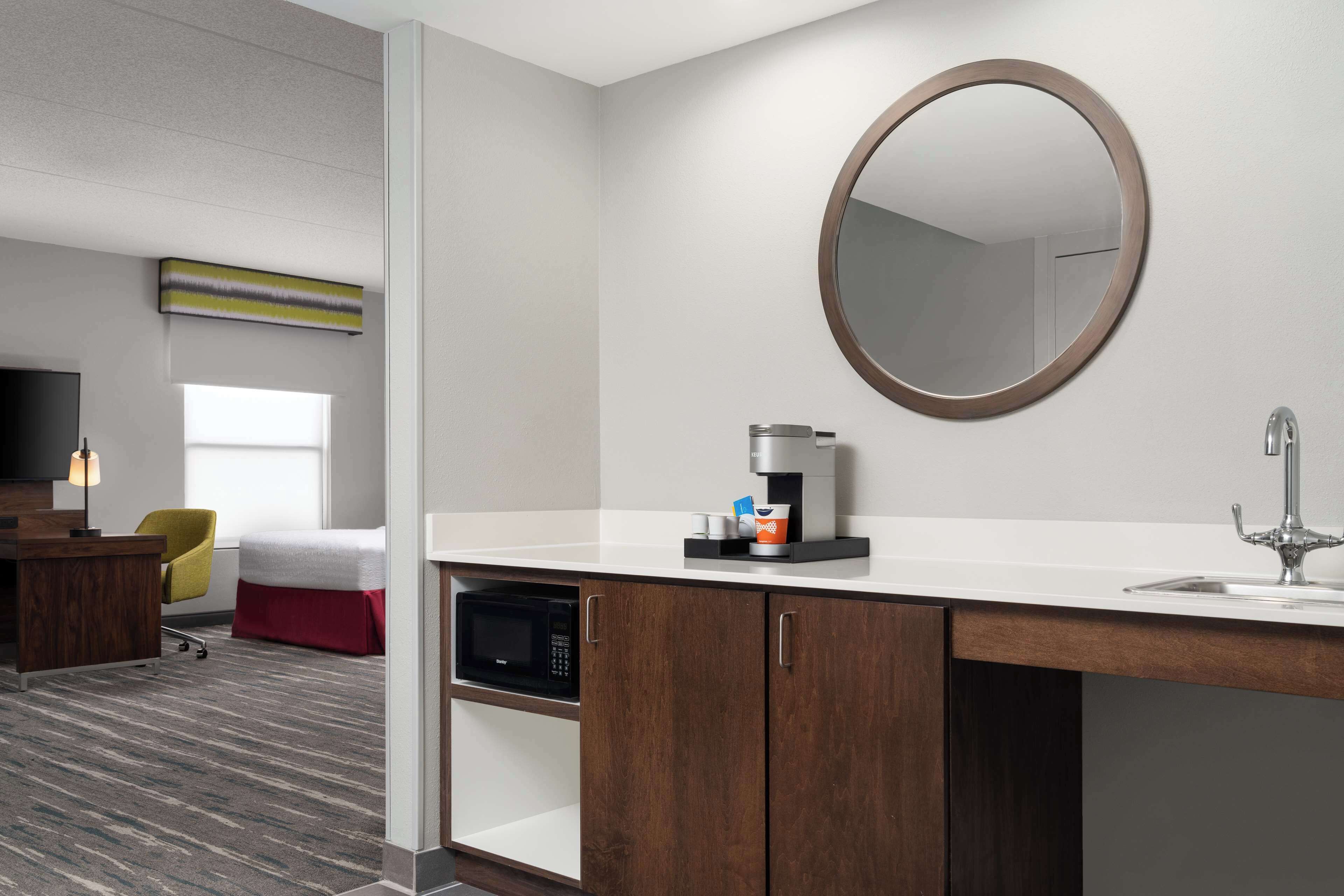 A hotel room with a white countertop, a coffee machine, a microwave, and a large mirror.