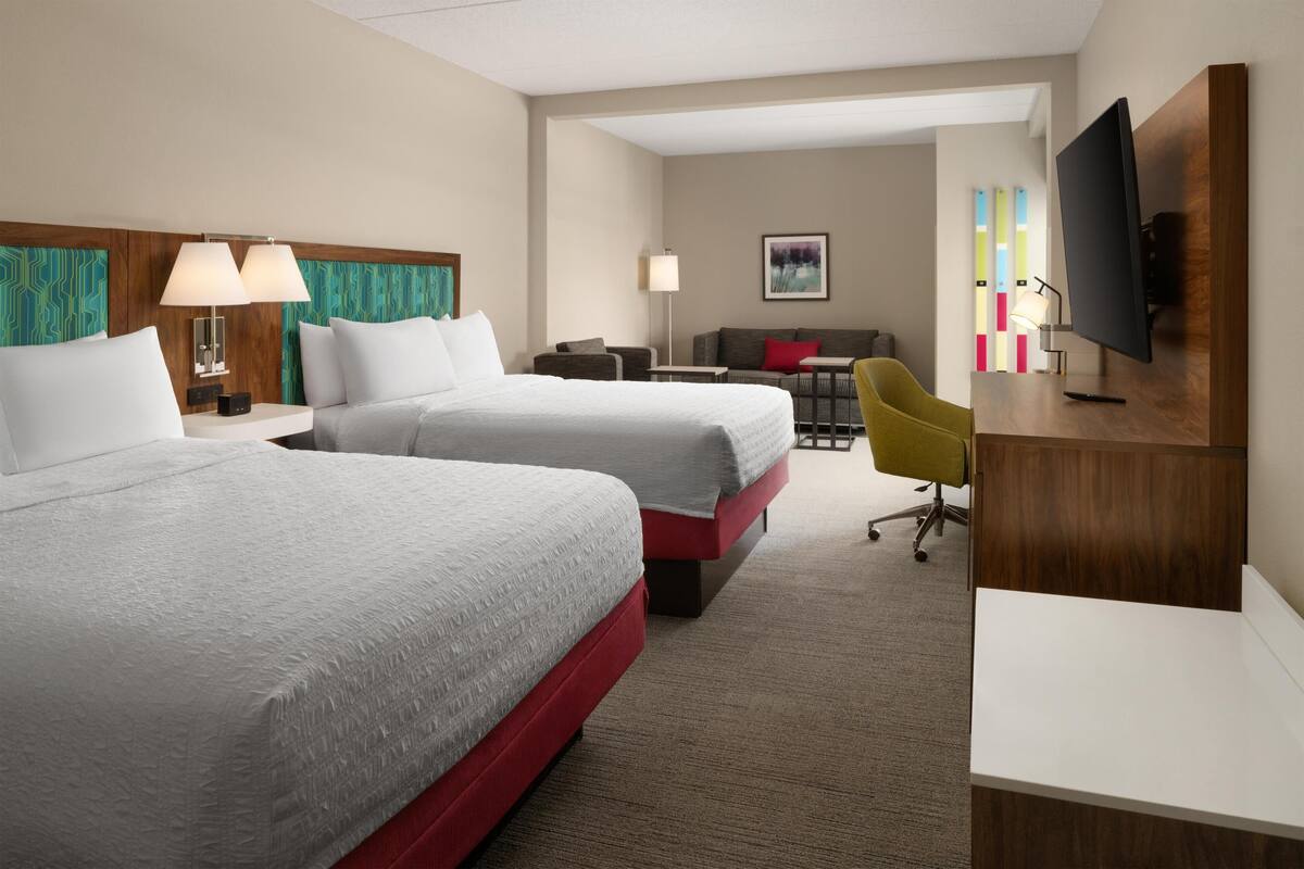 Ein Hotelzimmer mit zwei Betten, einem Schreibtisch, einem Fernseher und einem Sessel.