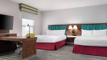 Habitación de hotel con escritorio, dos camas, televisor y ventana con cortinas.