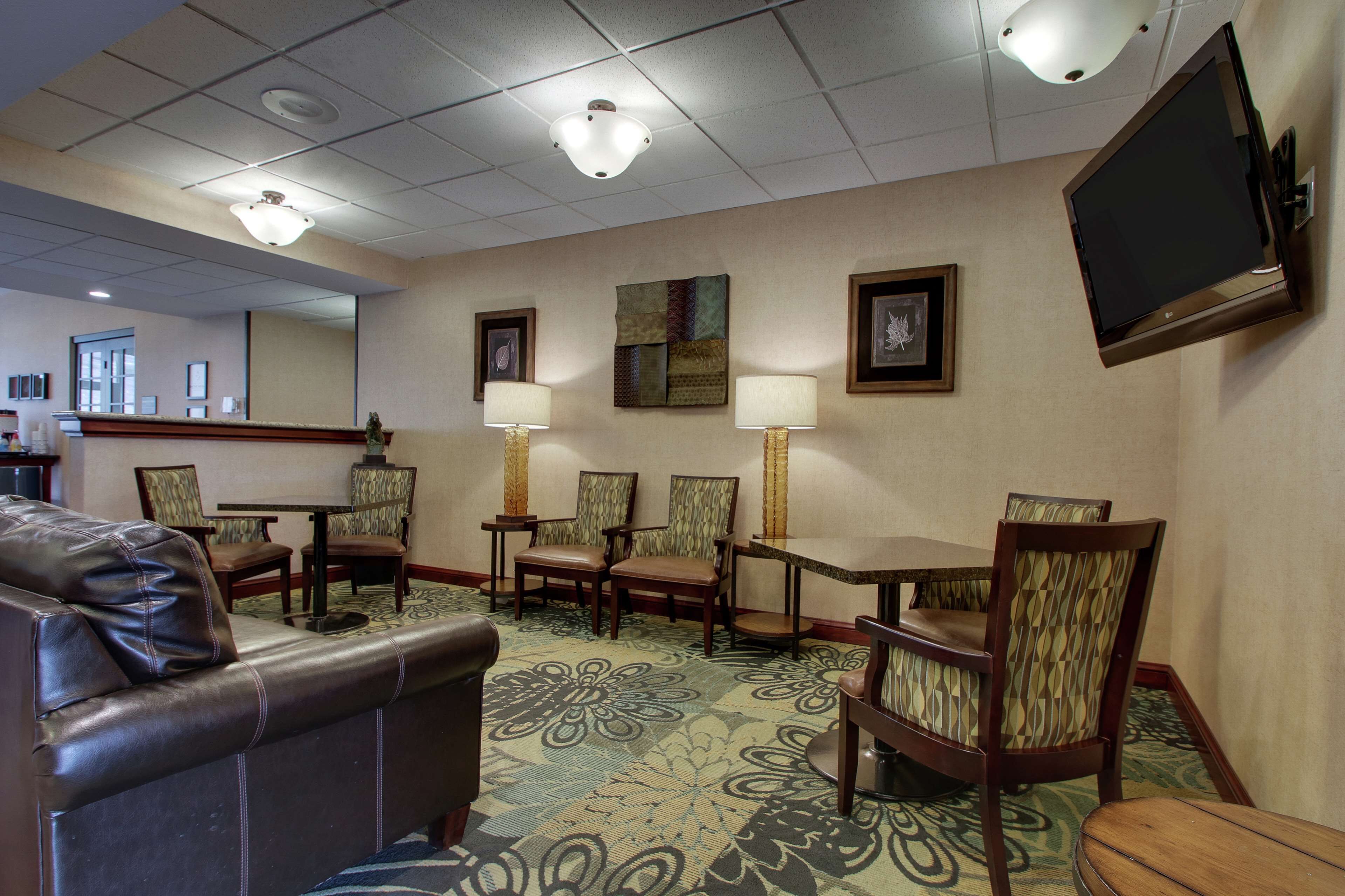 A hotel lobby with a leather sofa, dining table, chairs, and a flat-screen TV mounted on the wall.