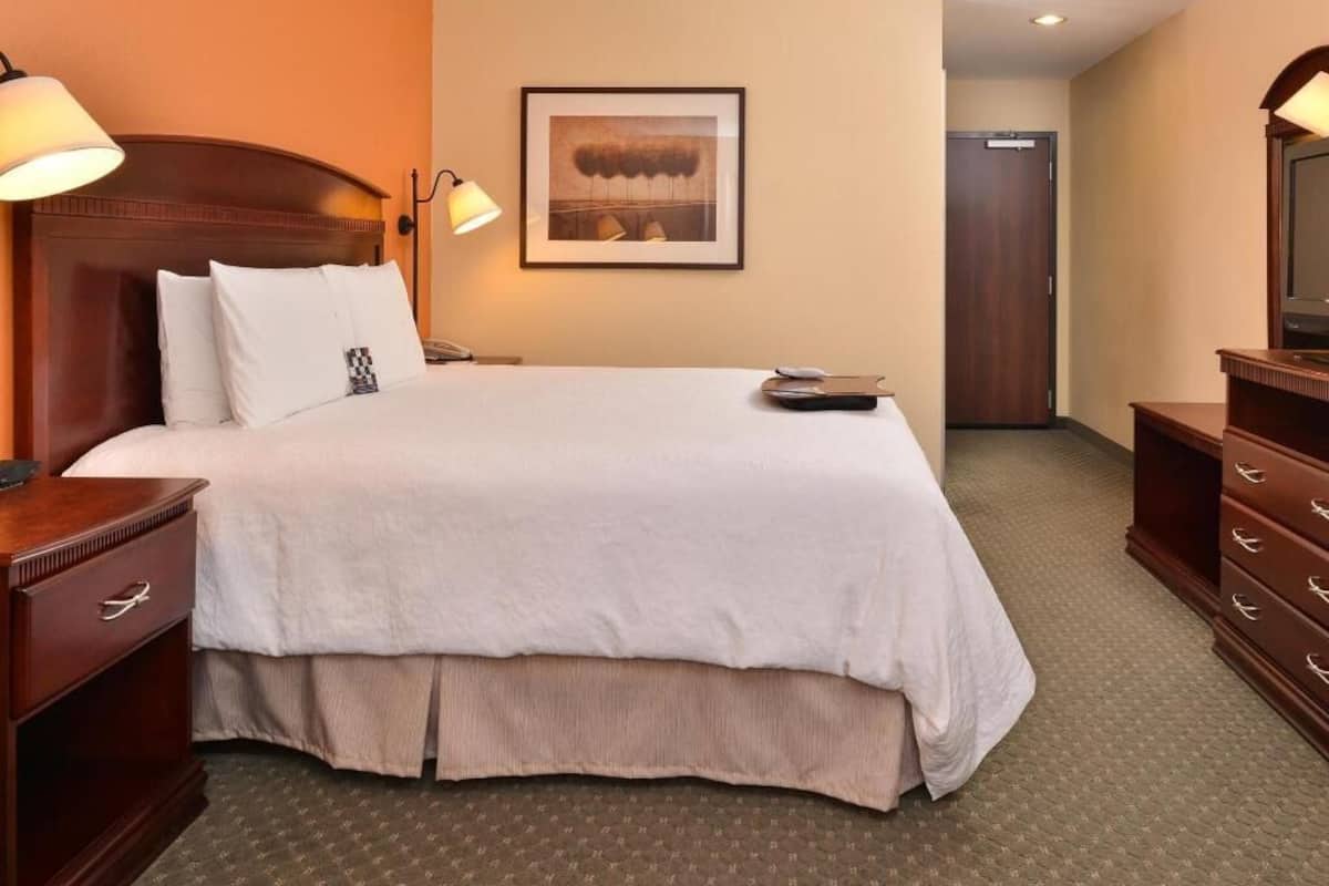 A hotel room with a large bed, bedside lamps, a framed picture on the wall, a dresser, and a door.