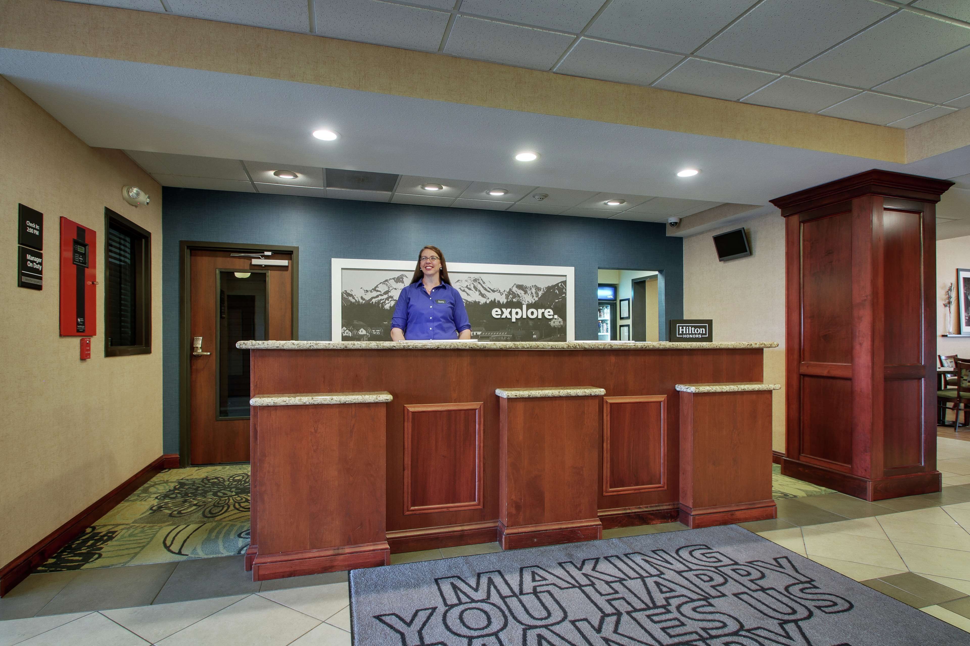 A hotel reception desk with a woman standing behind it, a large framed picture on the wall, and a sign that reads "explore."