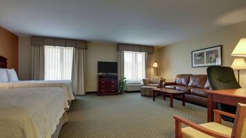 A hotel room with a bed, a sofa, a chair, a TV, and a lamp.