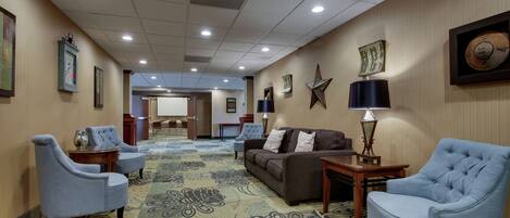 A hotel lobby with a carpeted floor, a sofa, two armchairs, a coffee table, and a lamp.