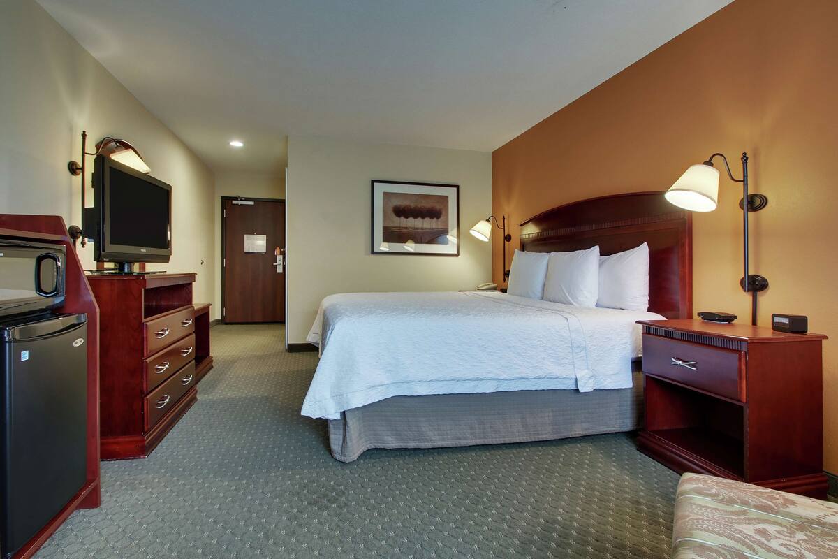 A hotel room with a bed, a desk, a television, and a dresser.