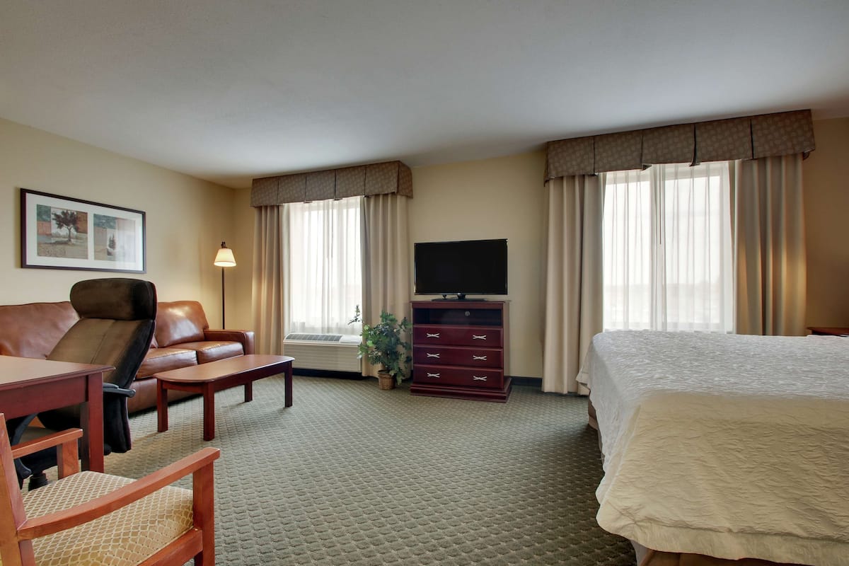 A hotel room with a bed, a sofa, a desk, a TV, and a dresser.
