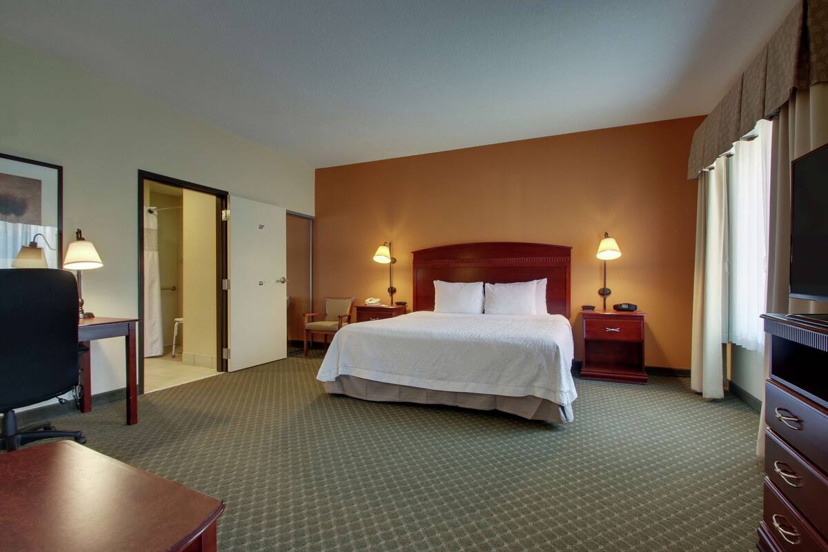 A hotel room with a large bed, two bedside tables with lamps, a desk, and a chair.