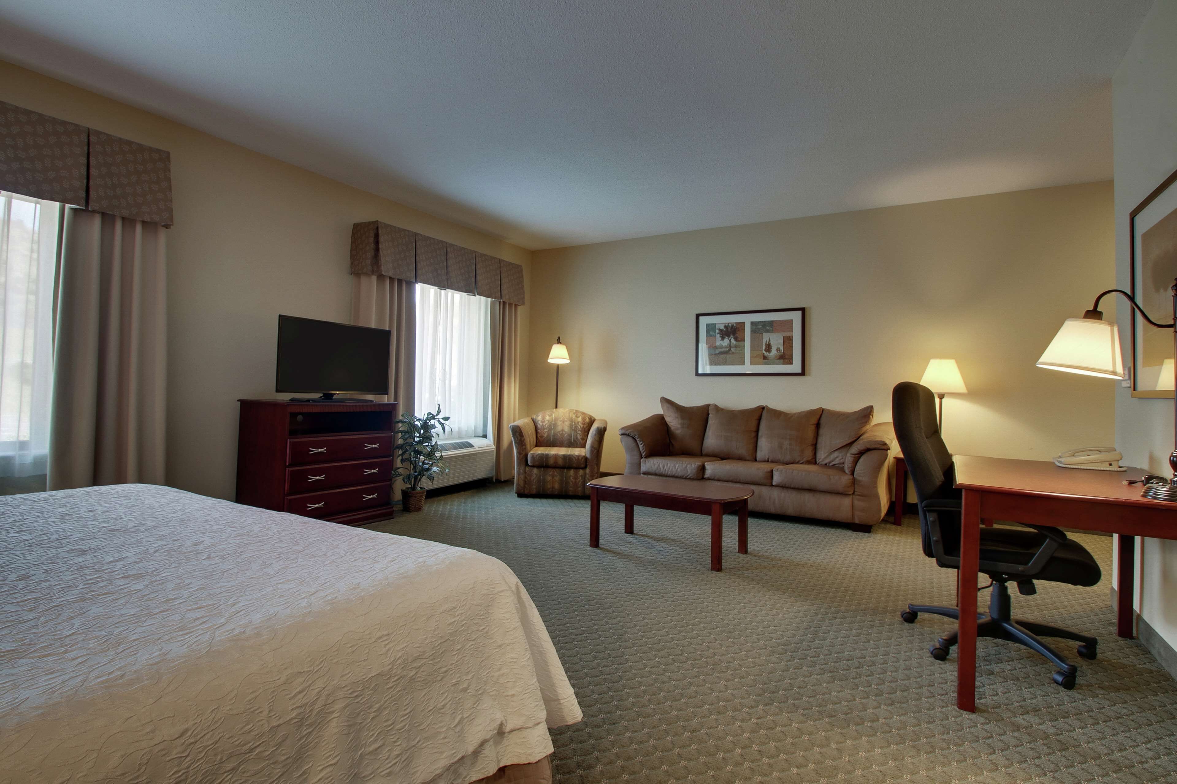 A hotel room with a large bed, a sofa, a desk with a chair, a television, and two lamps.