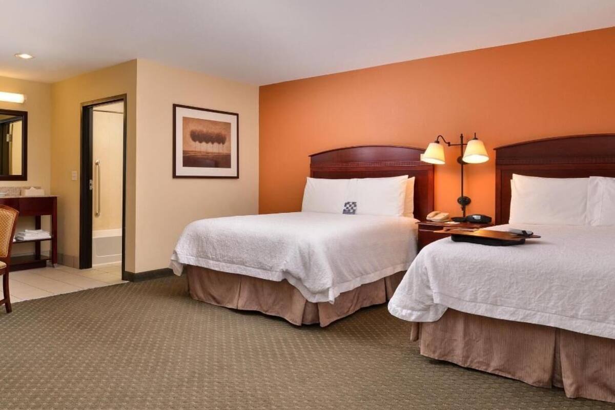 A hotel room with two beds, a desk, a chair, and a framed picture on the wall.