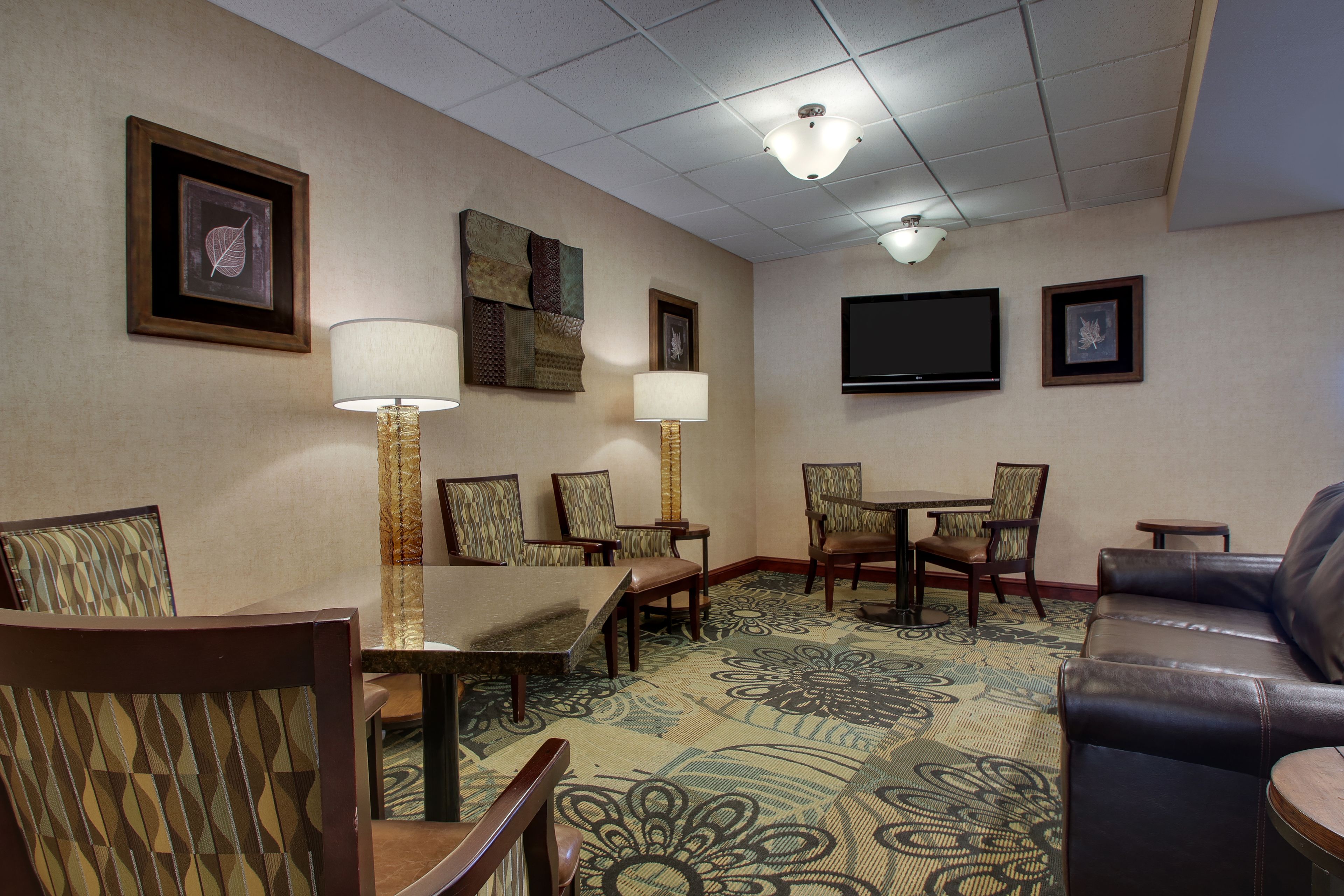 Habitación de hotel con una mesa de comedor, sillas, un sofá, un televisor y obras de arte en las paredes.